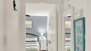 Un pasillo que conduce a un dormitorio con una cama, una mesita de noche y una lámpara de pared.