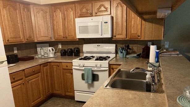 A kitchen with wooden cabinets, a white stove, a sink, and a microwave.