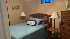 A bedroom with a bed, two bedside lamps, a dresser, and a window with curtains.