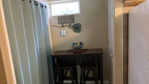 A small dining area with a table and two chairs, a 'hello' sign, a small plant, and a window with blinds.