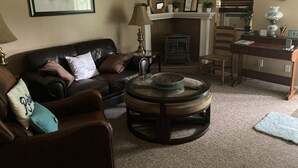 A living room with a leather couch, a round coffee table, a fireplace, a wooden desk, and a mirror on the wall.