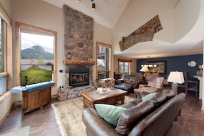 A spacious living room with a stone fireplace, leather sofas, a wooden coffee table, and a large window overlooking a mountainous landscape. - Corner Cascade Village Condo - Largest deck - Fire Pit - Views - Heated Pool (Durango)