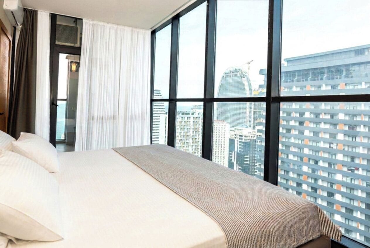 Ein Hotelzimmer mit einem großen Bett, Blick auf eine Stadtansicht und einem Vorhangfenster.