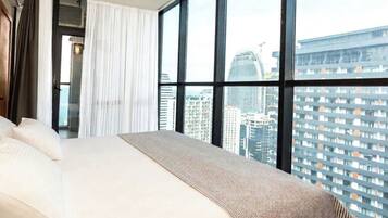 Ein Hotelzimmer mit einem großen Bett, Blick auf eine Stadtansicht und einem Vorhangfenster.