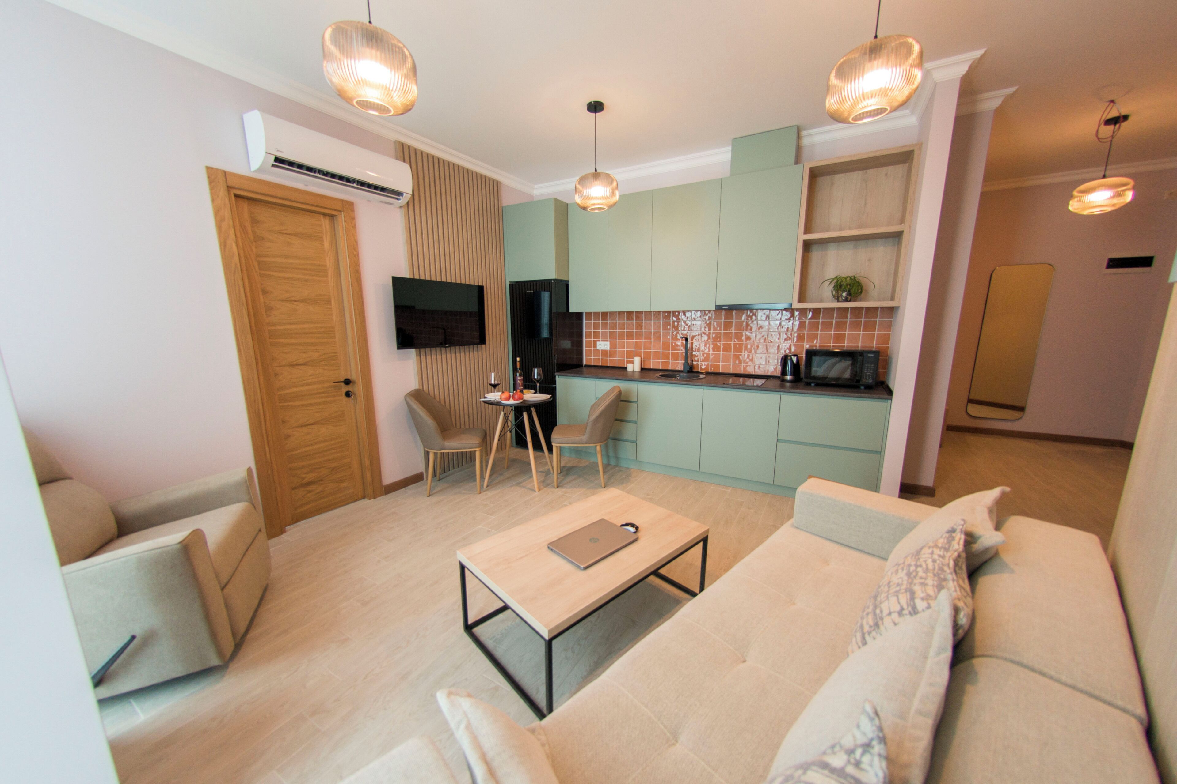 Una sala moderna con un sofá, una mesa de centro y sillas, una cocina con gabinetes verdes y un comedor con una mesa y sillas.
