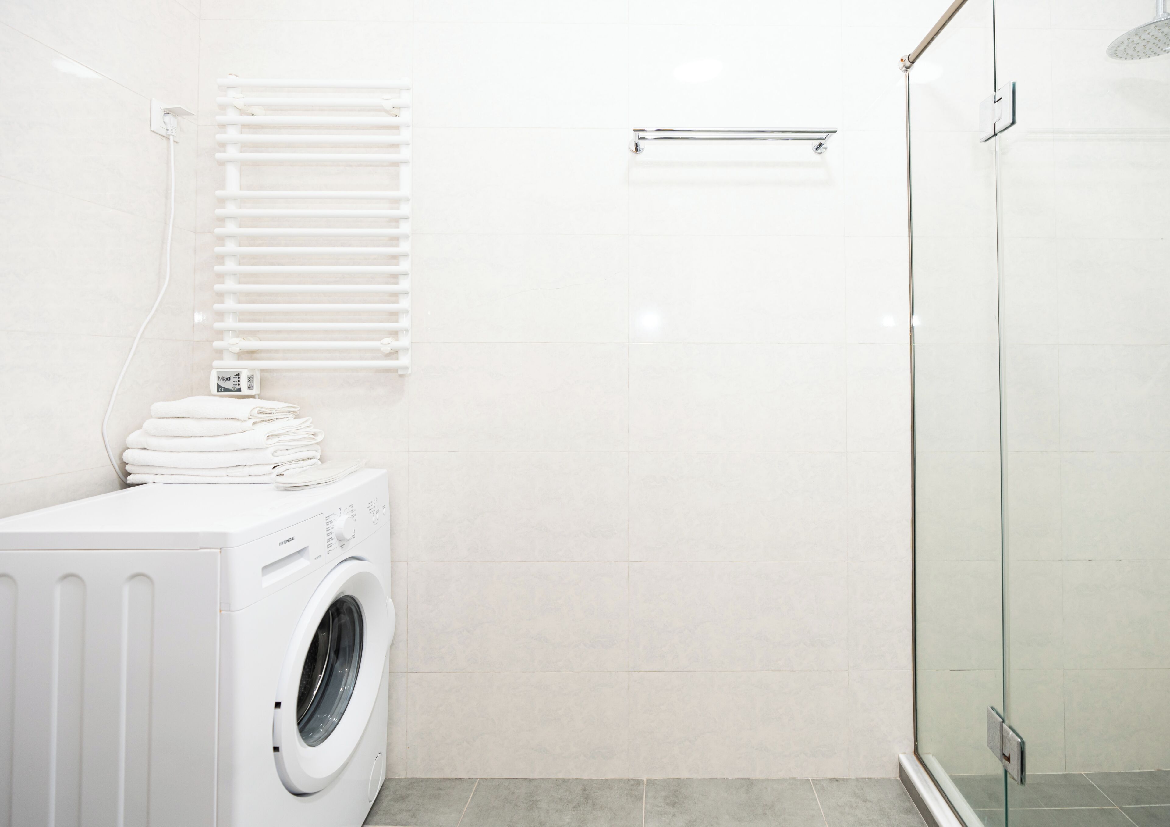A modern bathroom with a washing machine, a glass shower enclosure, and a towel rack.