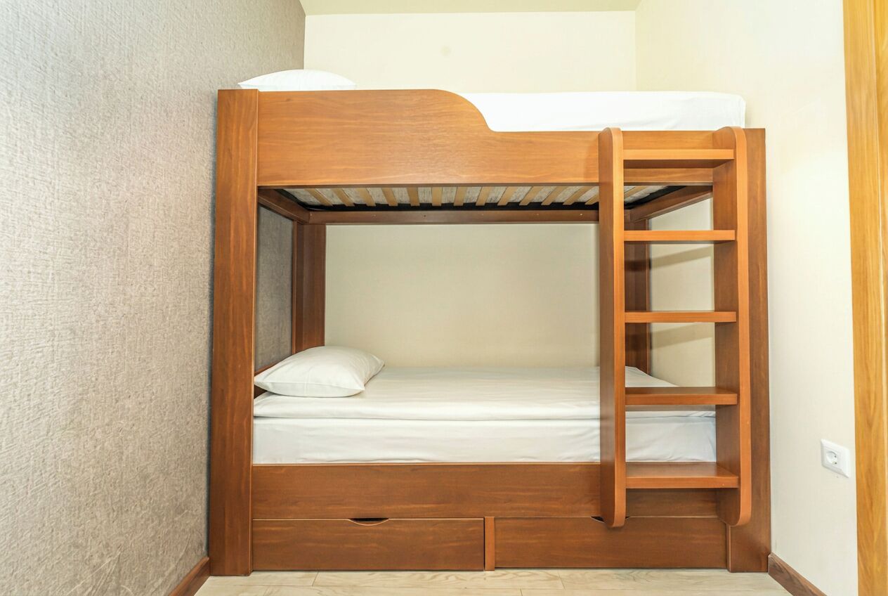 Een stapelbed met houten frame, een ladder en een enkel bed met kussen.
