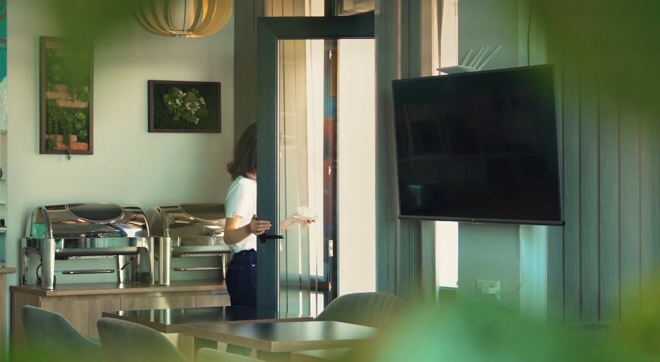 A modern kitchen with stainless steel appliances, a dining area with a table and chairs, and a large flat-screen TV mounted on the wall.