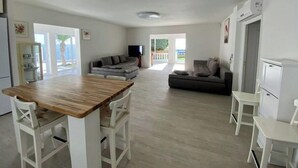 A modern kitchen with a wooden table and white chairs, a grey sofa, and a television in the background. - ¡nuevo! Villa Blanca. Besado por el sol y el Océano (Callao Salvaje)