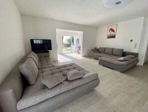 Un salon moderne avec un canapé d’angle, un téléviseur à écran plat et une grande fenêtre.