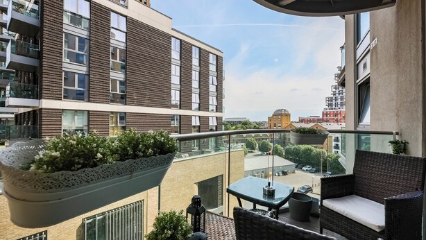 Ein Balkon mit Korbmöbeln, Blumentöpfen und Blick auf eine Stadtlandschaft.