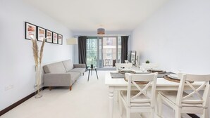 Ein modernes Wohnzimmer mit einer Couch, einem Esstisch und Stühlen. An der Wand befinden sich gerahmte Zertifikate und eine Vase mit Pampasgras.