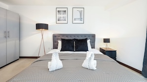 Ein Schlafzimmer mit einem Bett, zwei gerahmten Bildern an der Wand, einem Nachttisch und einer Lampe.