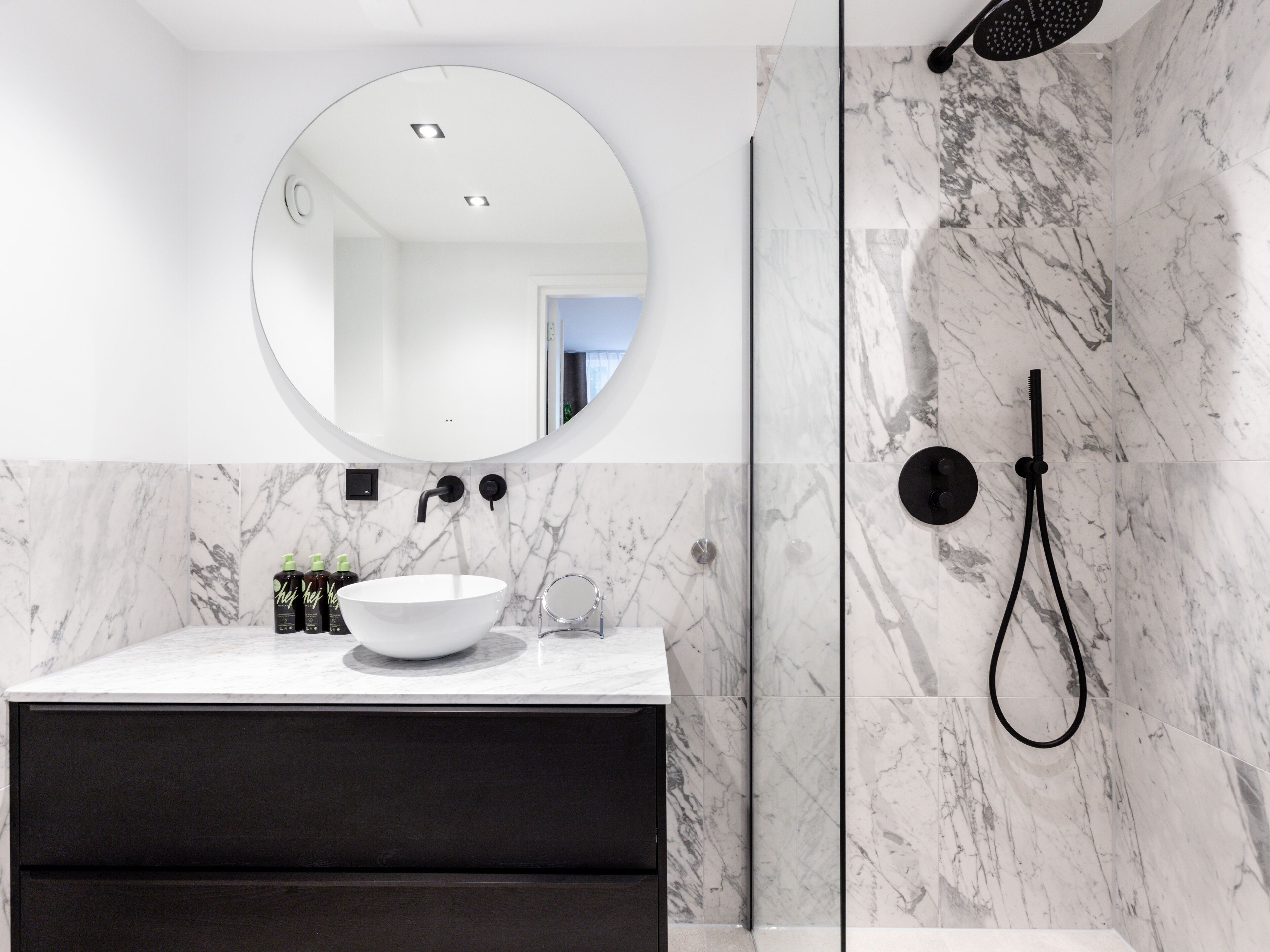 Un baño moderno con un espejo redondo, un lavabo blanco y un cabezal de ducha de mano.