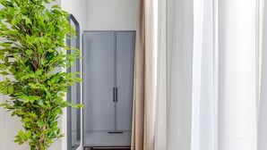 Ein Flur mit einer Topfpflanze, einem grauen Kleiderschrank und einer weißen Tür mit Vorhängen.
