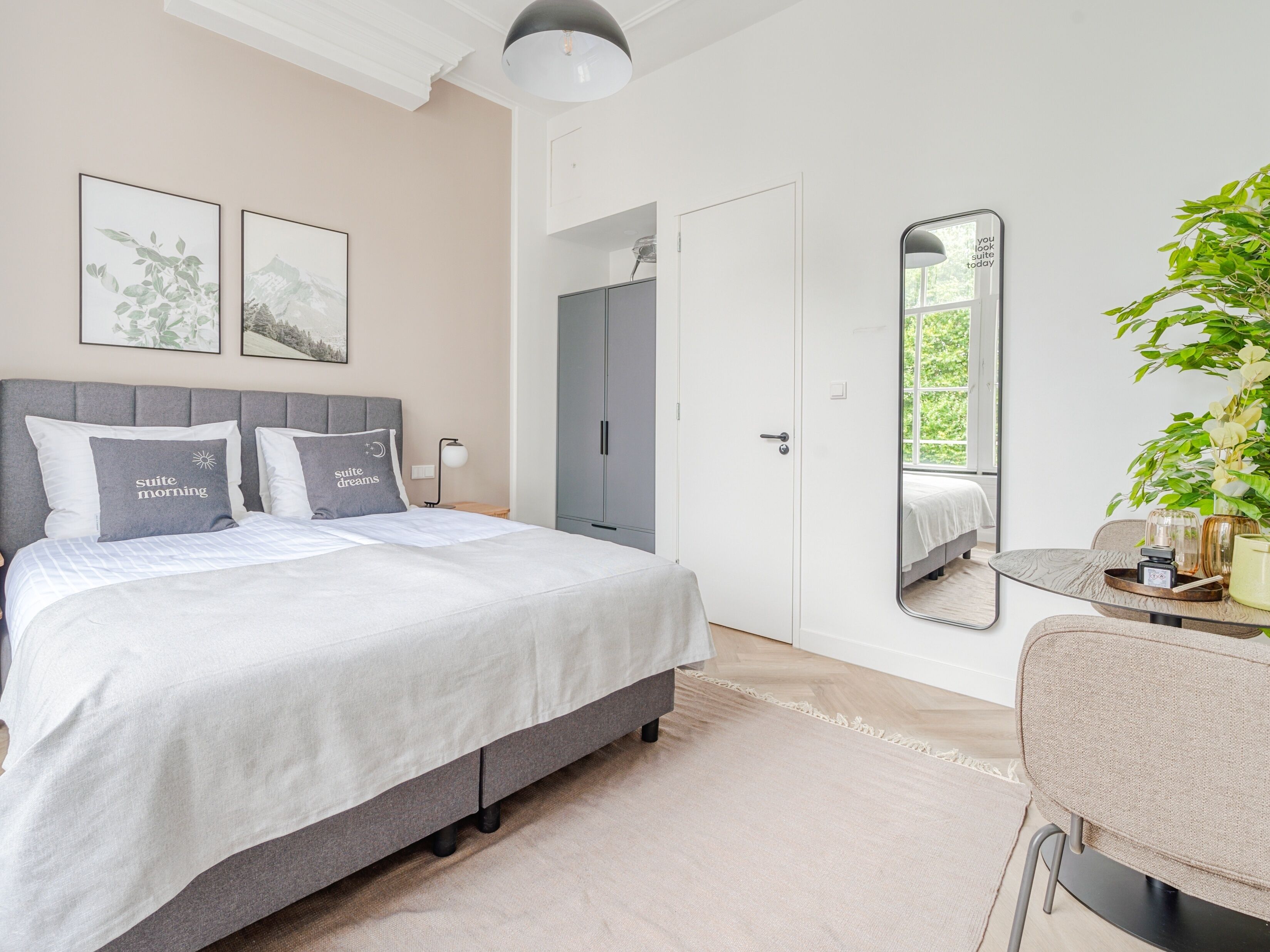 A modern bedroom with a bed, bedside tables, a mirror, and a potted plant.