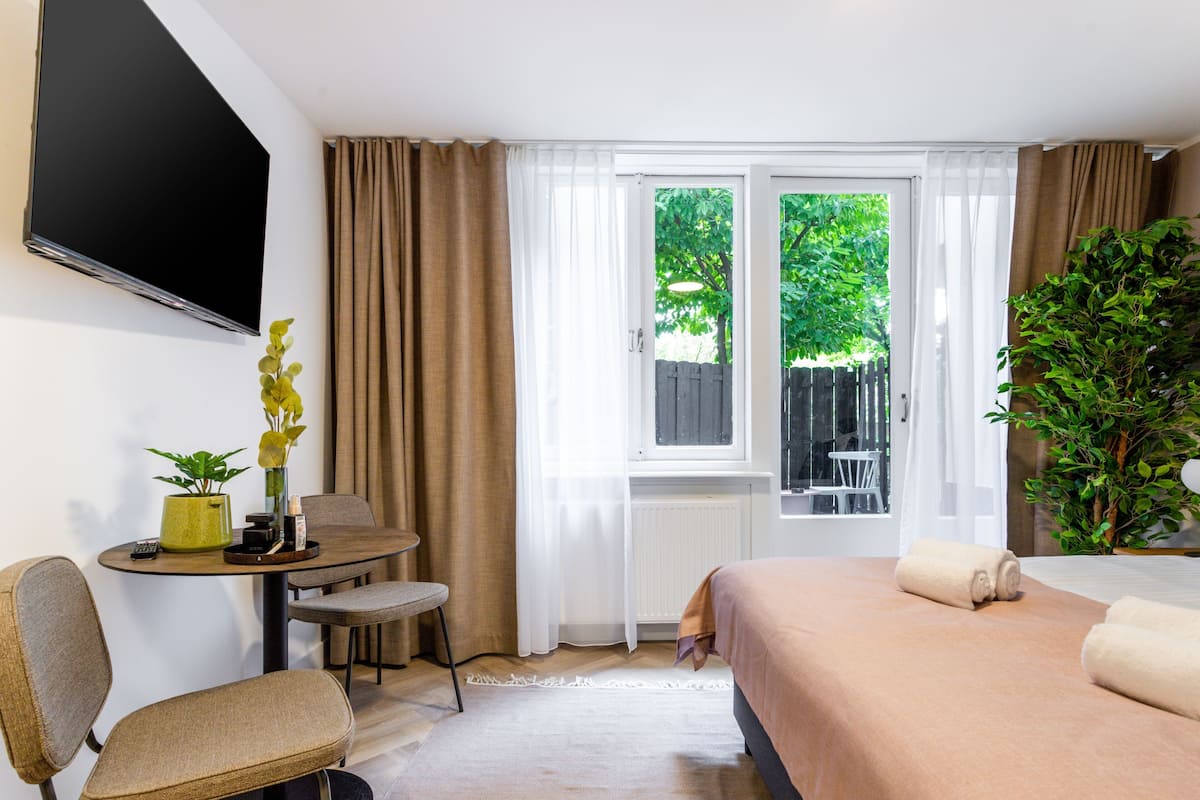 Ein Hotelzimmer mit einem Bett, einem Schreibtisch mit Stuhl, einem Fernseher, einem Fenster mit Vorhängen und einer Zimmerpflanze.