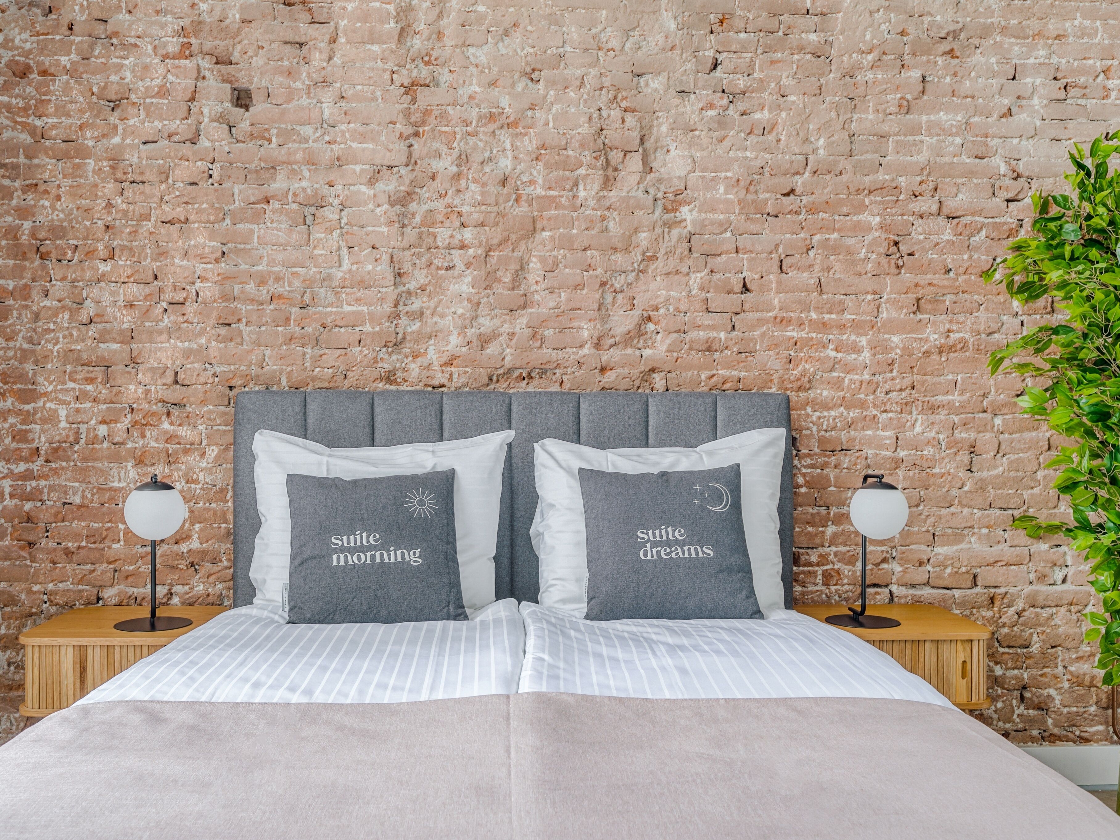 Una cama con dos almohadas, un muro de ladrillo y dos lámparas de noche.