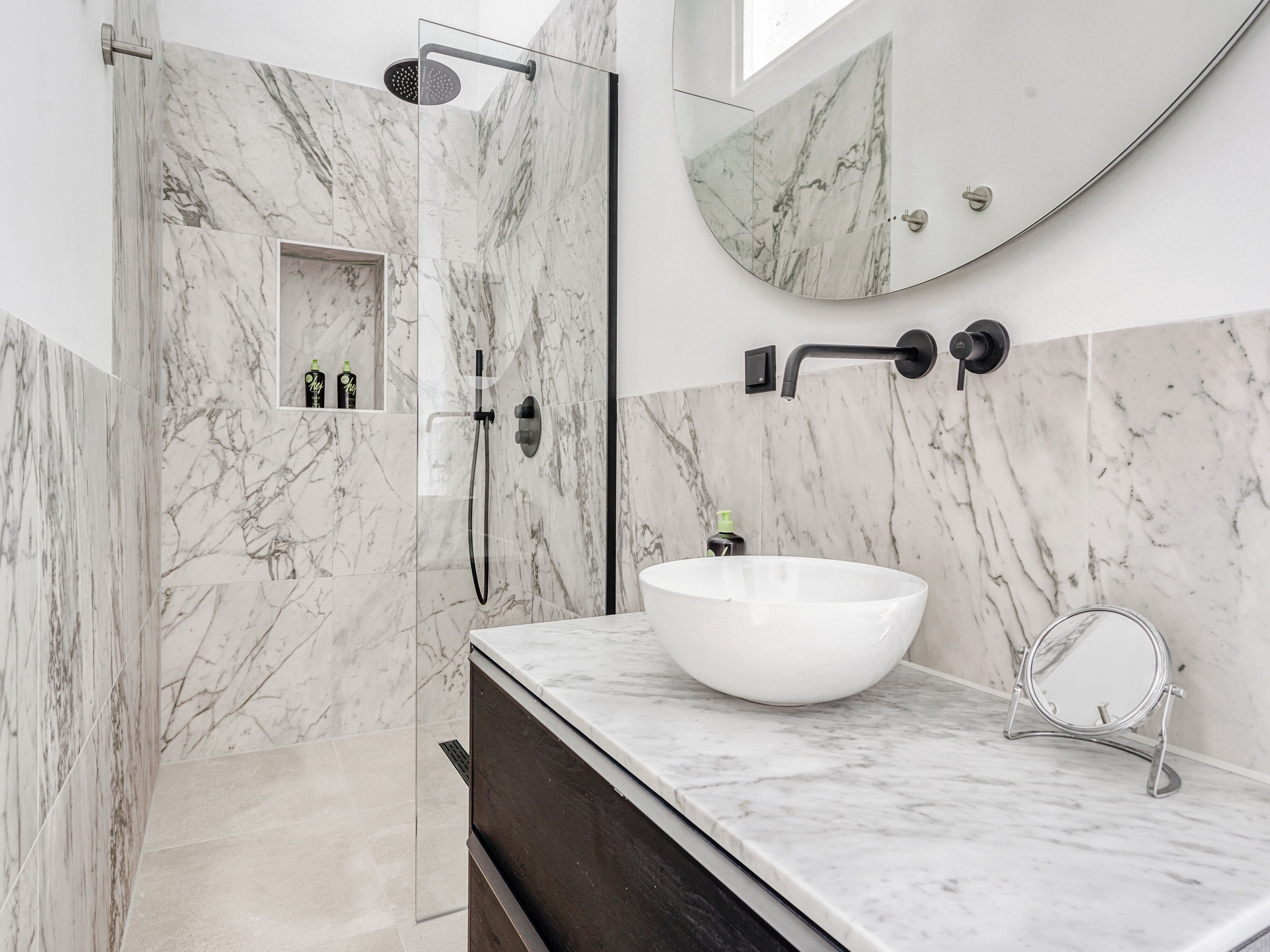 A modern bathroom with a large white vessel sink, a handheld showerhead, and a mirror.