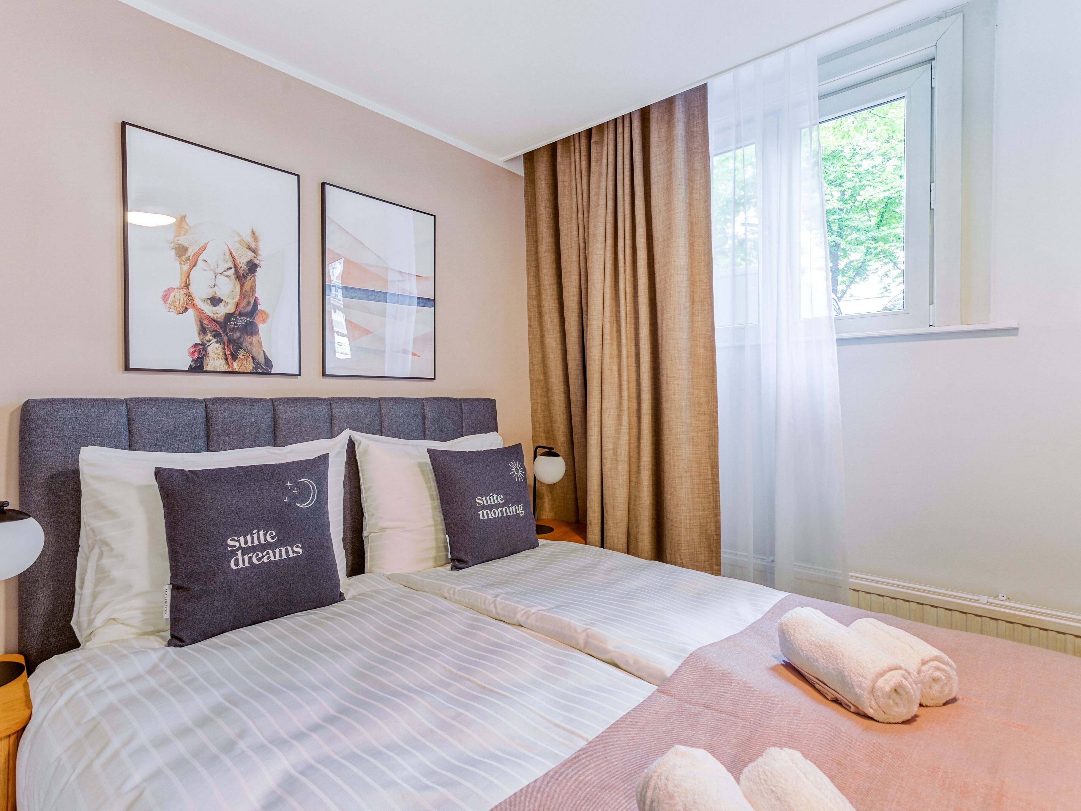 A hotel room with two beds, a large window with curtains, and artwork on the wall.