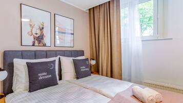 A hotel room with two beds, a large window with curtains, and artwork on the wall.