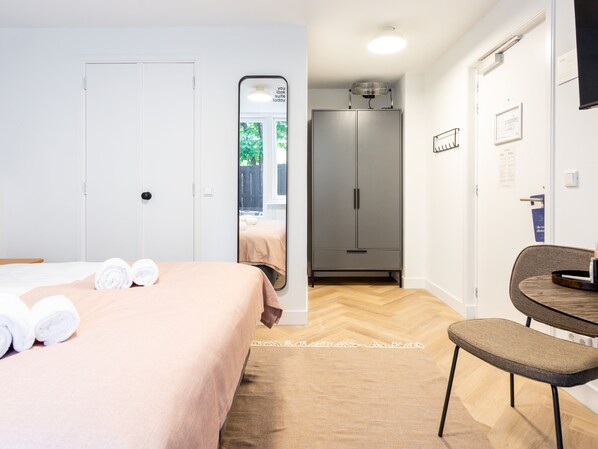 A hotel room with a bed, a chair, a wardrobe, and a mirror.