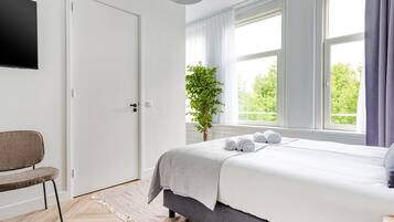 A bedroom with a bed, a chair, a plant, and a TV on the wall.
