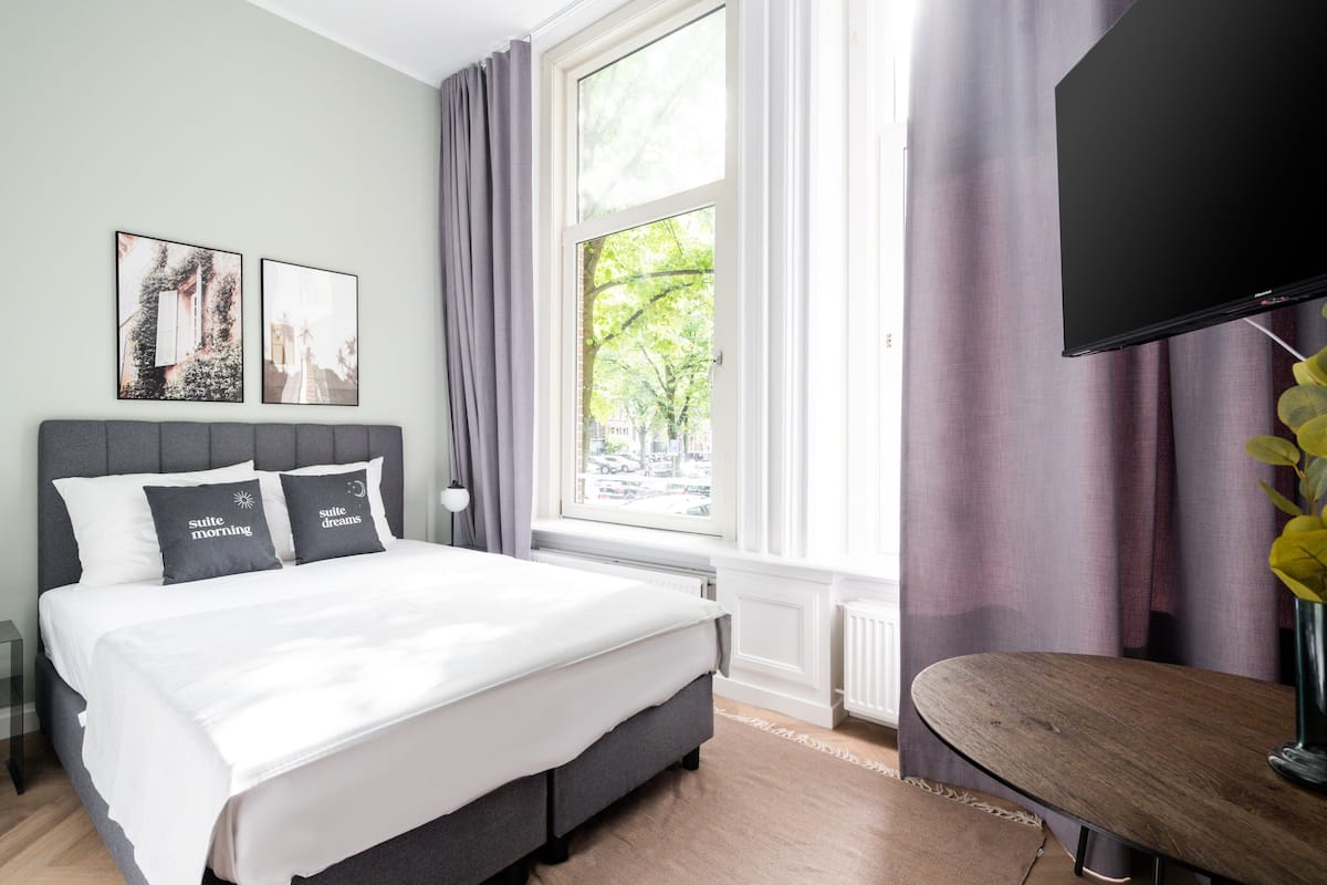 Ein modernes Schlafzimmer mit einem Bett, einem Flachbildfernseher und einem Fenster mit Vorhängen.
