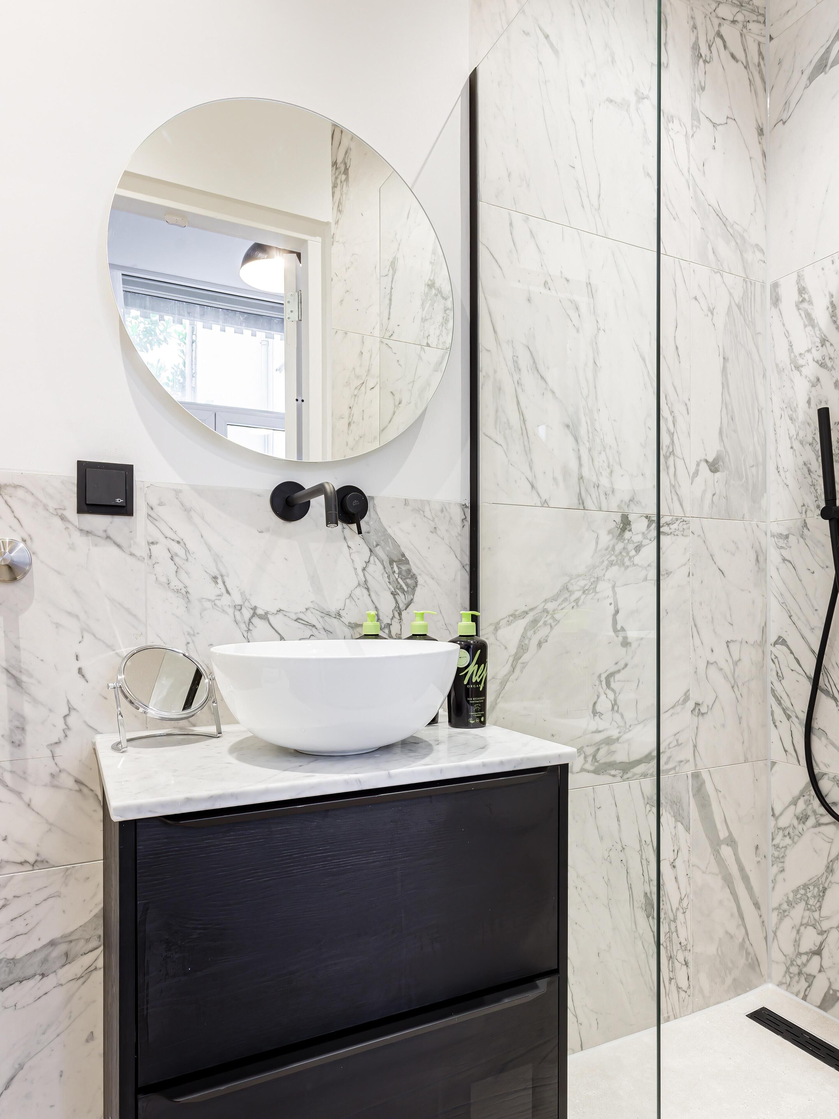 A bathroom with a white marble sink, a round mirror, and a black cabinet.
