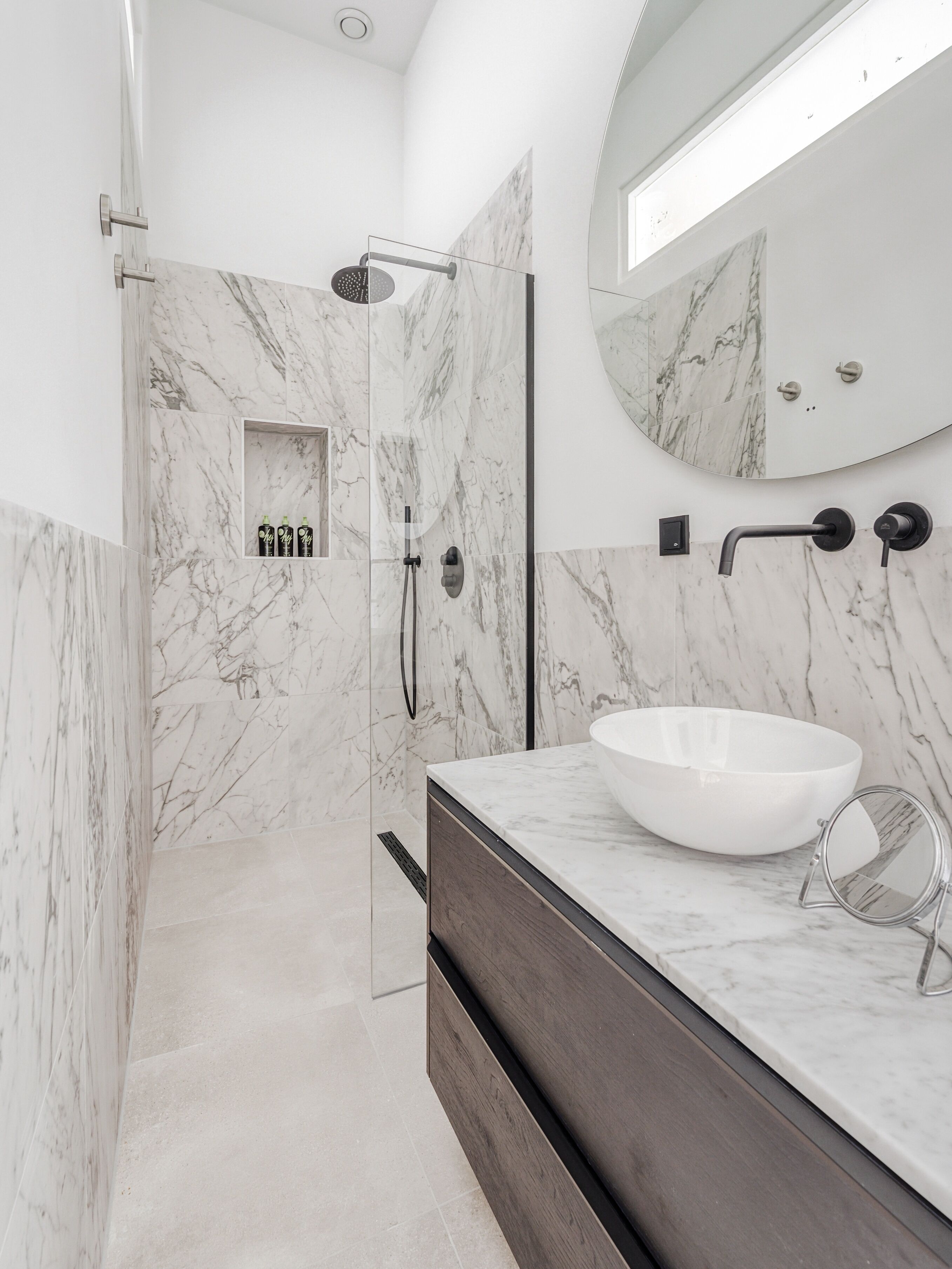Une salle de bain moderne avec une douche à parois de verre, un grand lavabo blanc et un mur recouvert de carreaux de marbre.