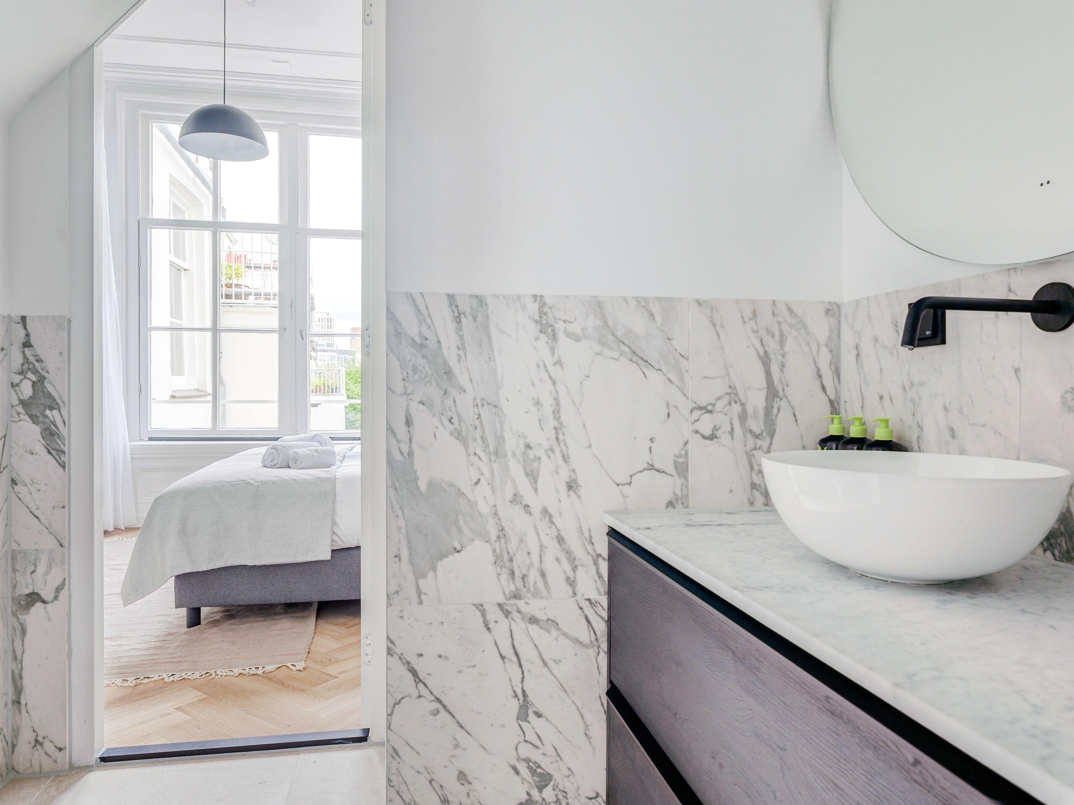 Een moderne badkamer met een witte wastafel, marmeren wanden en een grote spiegel.