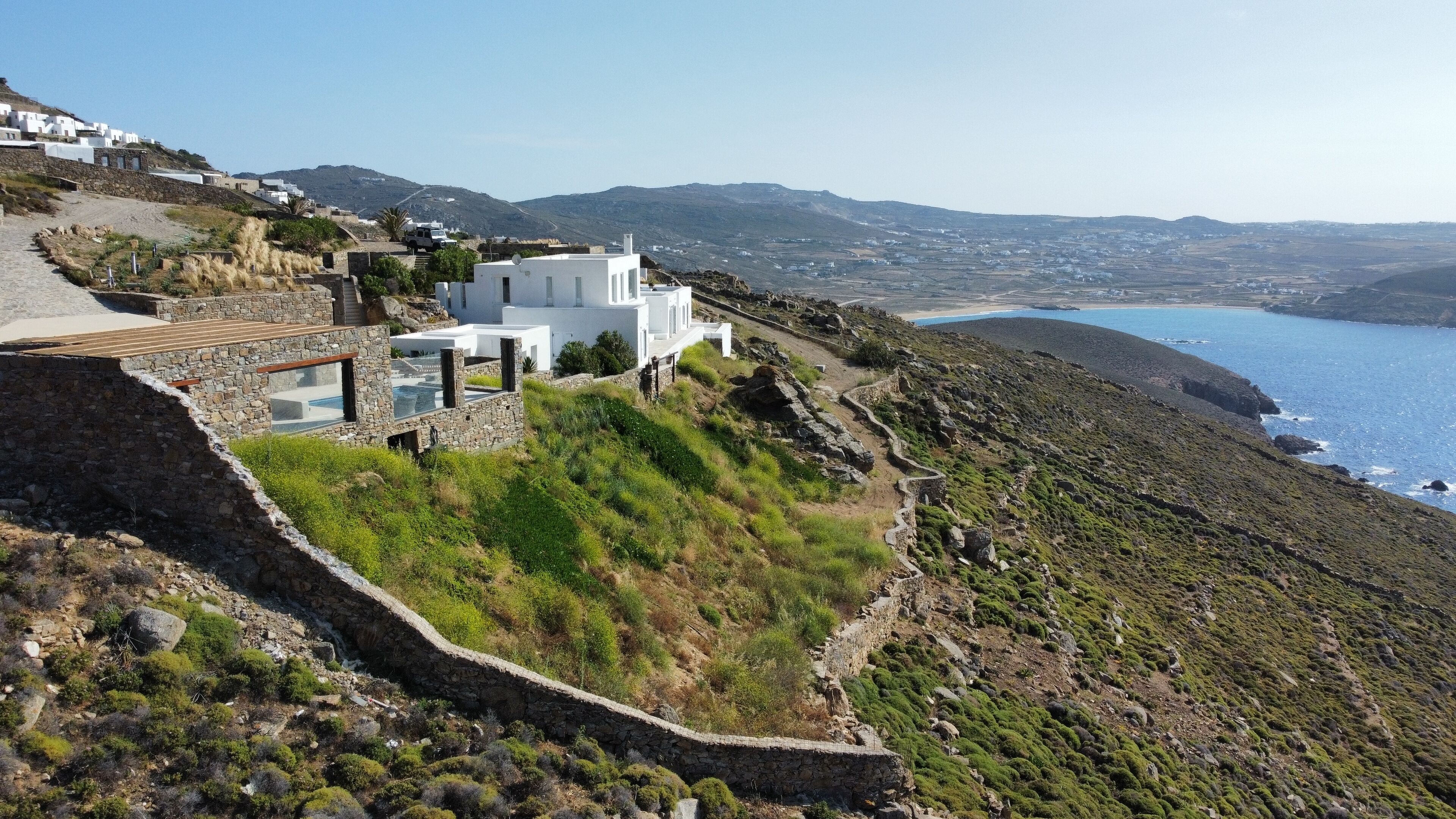 A white building with a stone pathway leading to a pool, overlooking a coastal landscape.
