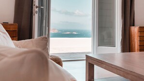 Een hotelkamer met een bed, een houten nachtkastje en een tafel. De kamer heeft een groot schuifglas dat leidt naar een balkon met uitzicht op zee.