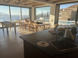 Une cuisine moderne dotée d’un grand îlot central, d’un coin repas avec des chaises et offrant une vue sur la mer et les montagnes.