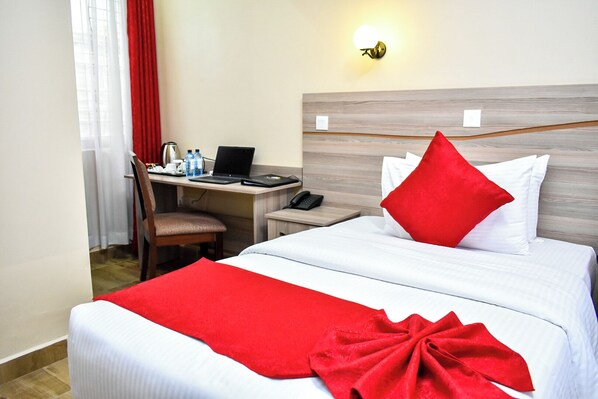 A hotel room with a bed, a desk with a laptop, a chair, and a telephone.