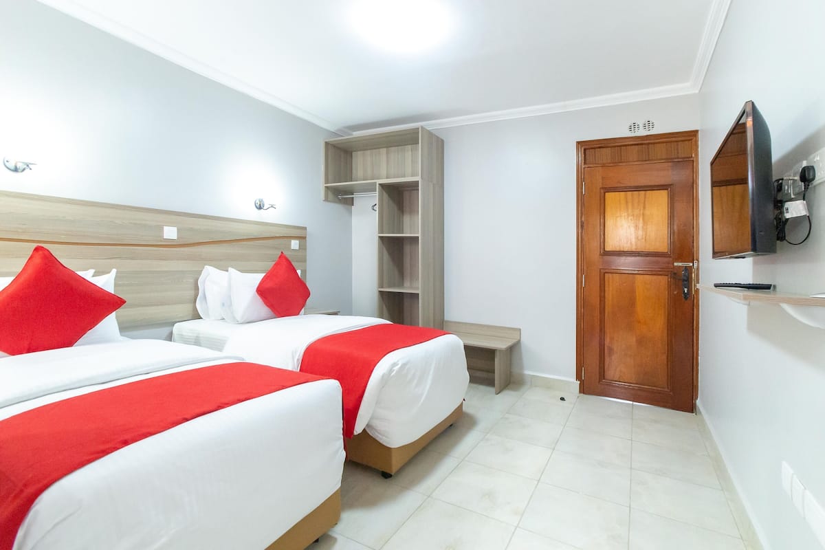 A hotel room with two beds, a wooden wardrobe, a television, and a door.