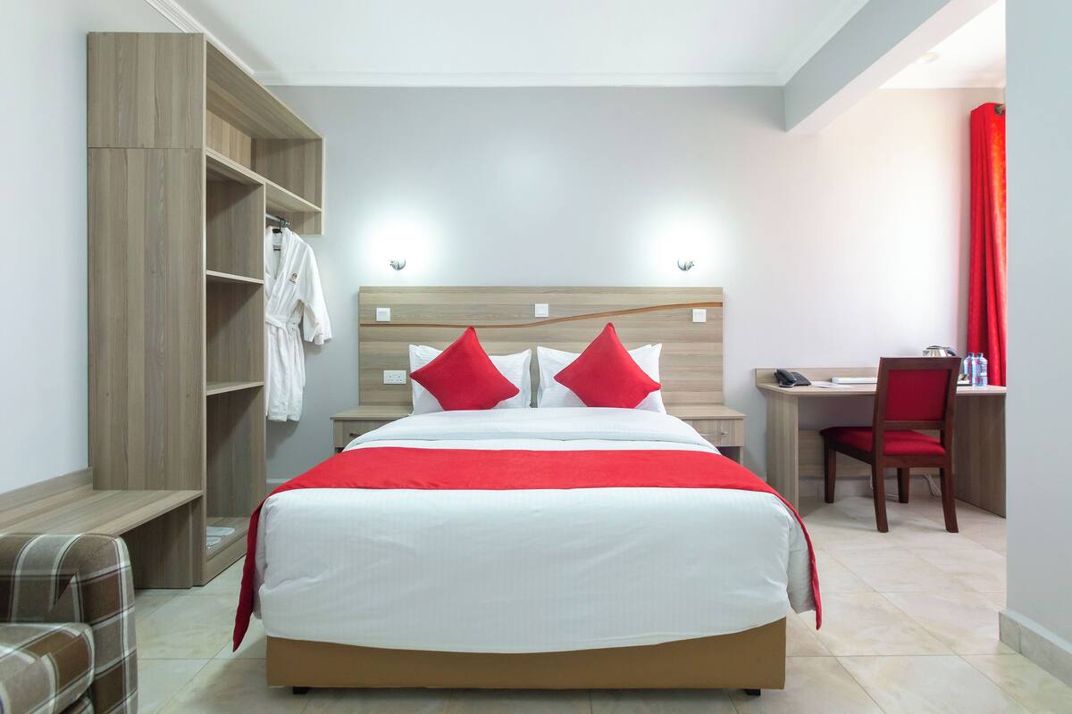 A hotel room with a bed, a desk, a chair, and a wardrobe.