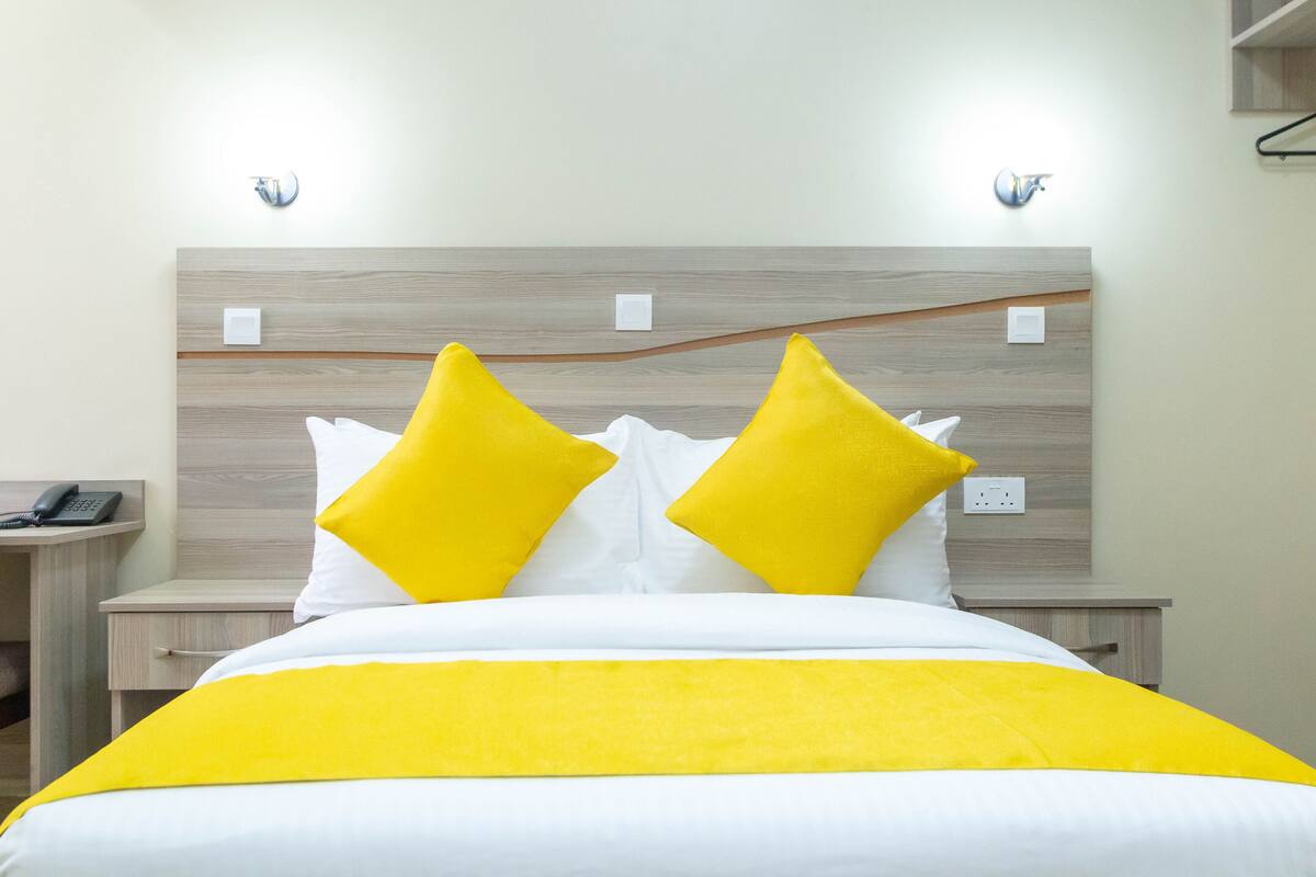 A hotel room with a bed, two bedside tables, a nightstand, and a wall-mounted light fixture.