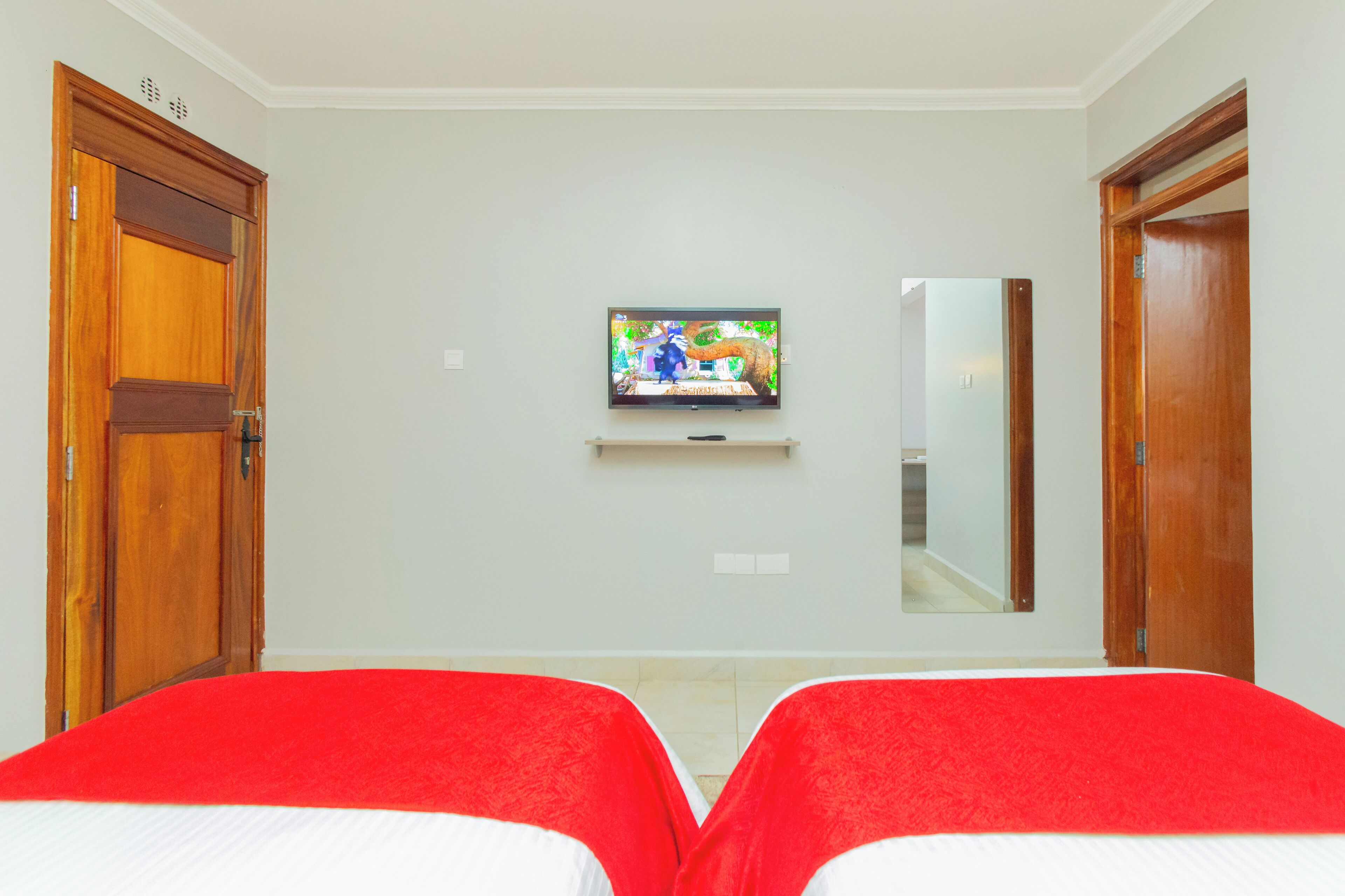 Ein Hotelzimmer mit zwei Betten, einem an der Wand befestigten Fernseher und Holztüren.
