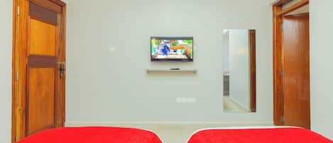 A hotel room with two beds, a television on the wall, and wooden doors.