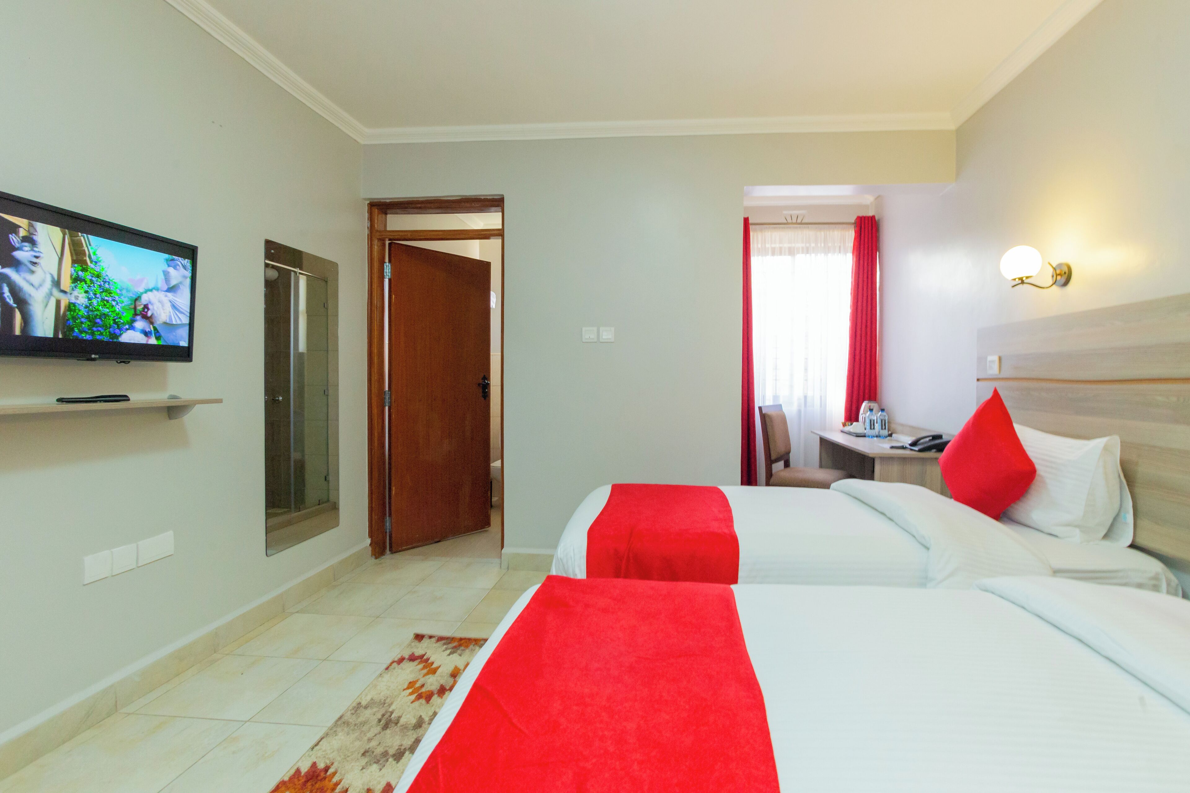 A hotel room with two beds, a television on the wall, a desk with a chair, and a bathroom door.