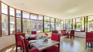A restaurant with large windows, red chairs, and a tiled floor. - Rock Hyrax Hotel (Nakuru)