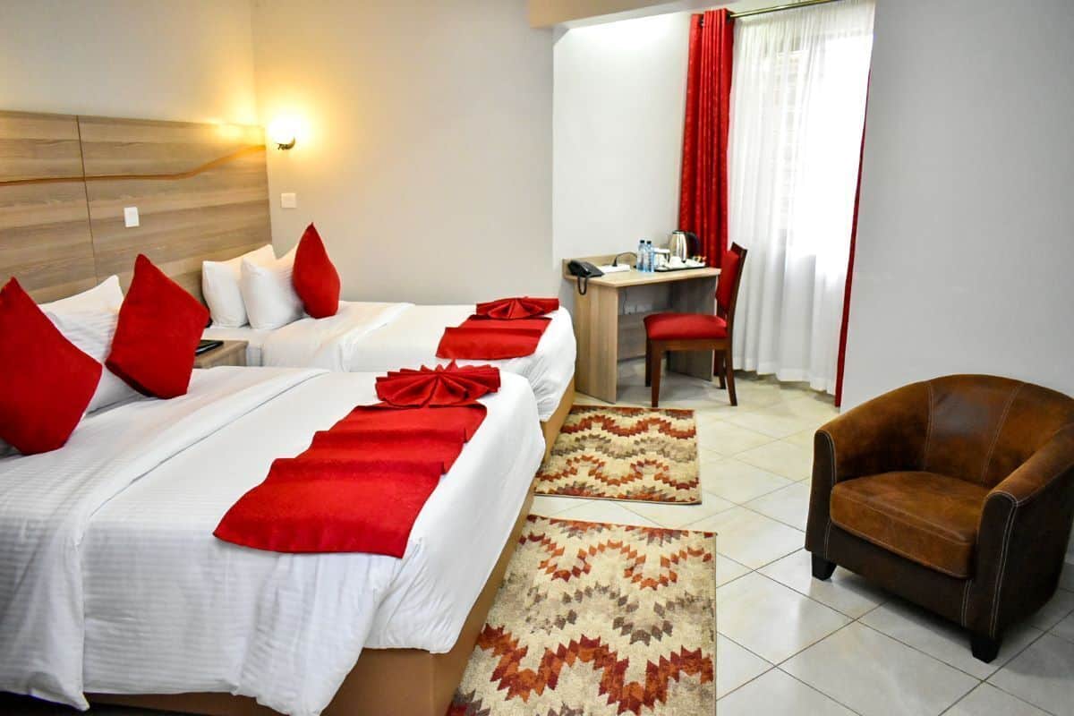 A hotel room with two beds, a desk, a chair, and a rug.