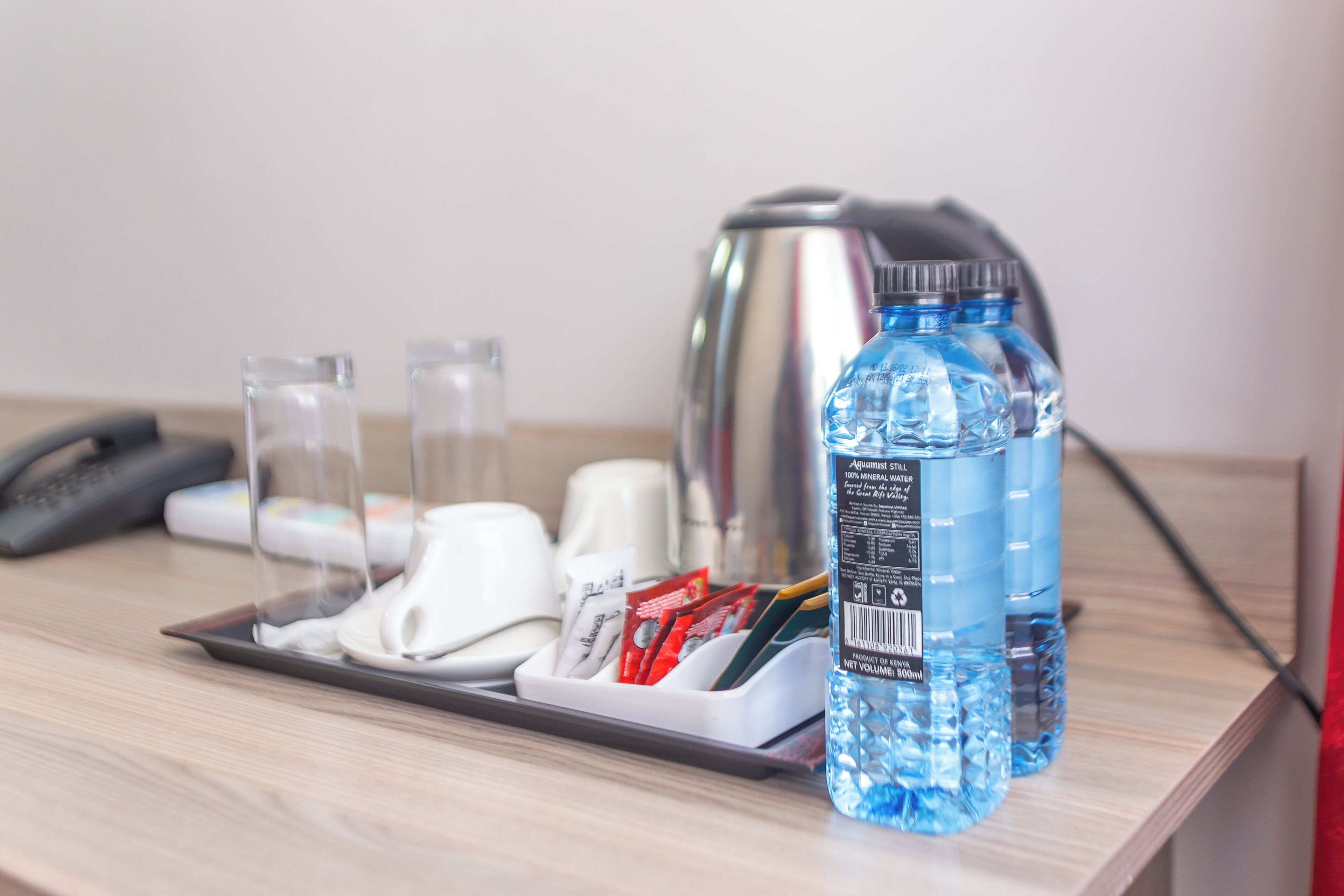 Een hotel bureau met een waterkoker, waterflesjes, een telefoon en een tissuespender.