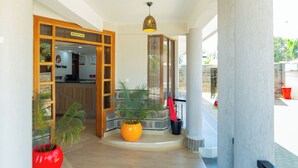 A reception area with a reception desk, a clock, and a sign indicating the reception. There are potted plants and a staircase leading to an upper level. - Rock Hyrax Hotel (Nakuru)