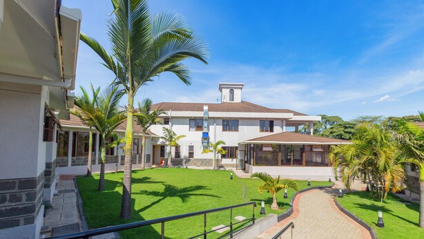A two-story building with a paved pathway leading to a covered area, surrounded by well-maintained grass and palm trees. - Rock Hyrax Hotel (Nakuru)