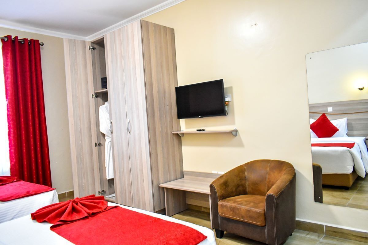 Ein Hotelzimmer mit einem Bett, einem roten Handtuch, einem braunen Sessel, einem Fernseher und einem Kleiderschrank.