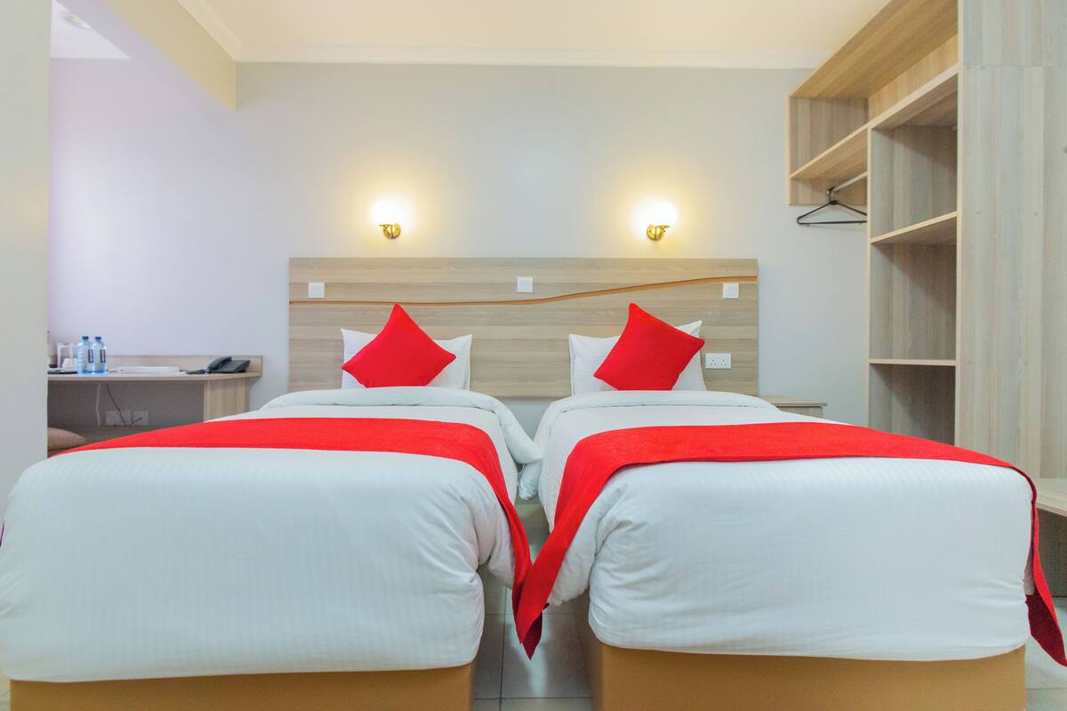 A hotel room with two beds, each with red and white bedding, a wooden headboard, and two wall-mounted lights.