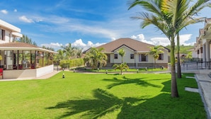 A residential area with a house, a covered patio, and a well-maintained lawn with palm trees. - Rock Hyrax Hotel (Nakuru)