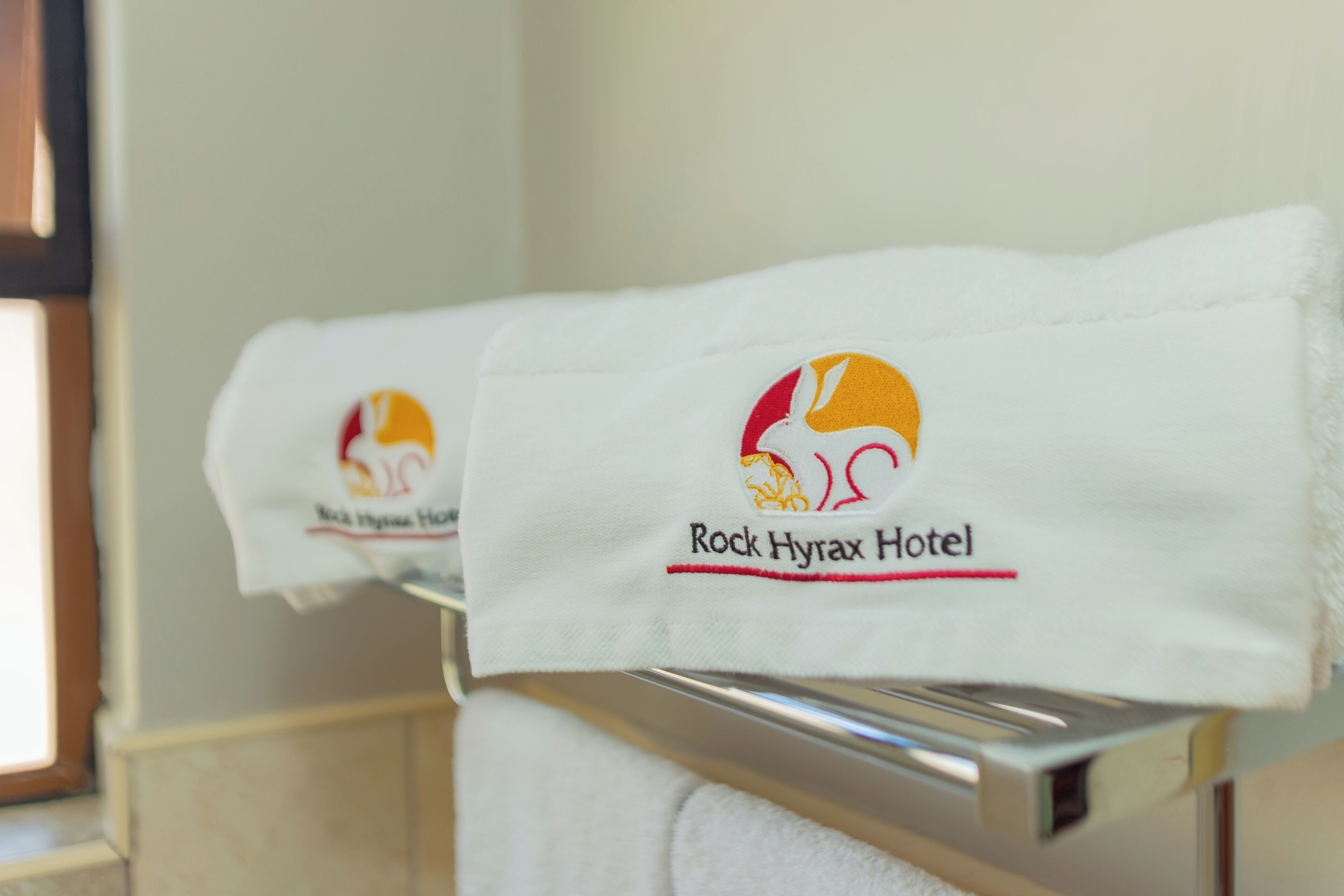 Une serviette ornée du logo de l’hôtel Rock Hyrax, posée sur un porte-serviettes en métal dans une chambre d’hôtel.